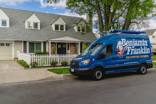 A blue Benjamin Franklin Plumbing van in front of a Miami FL home