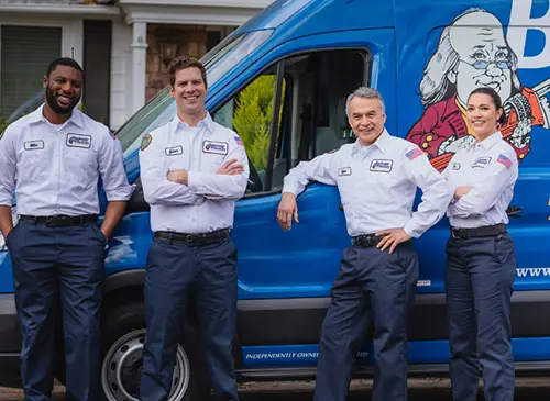 Team of four Benjamin Franklin Plumbing Techs standing in front of blue service van